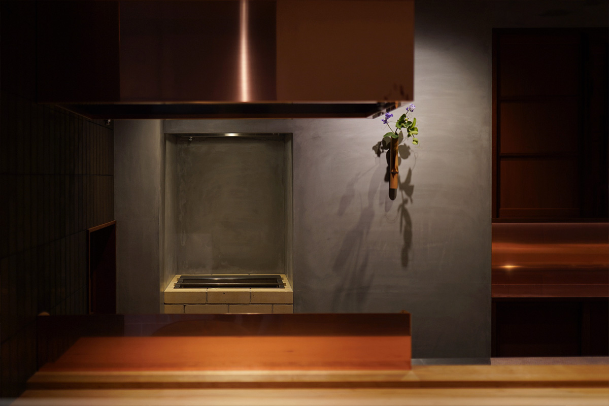 レンガの造作炭焼き台と銅板フード「近野」店内。グレー漆喰、生花が映える京都の和モダン内装。