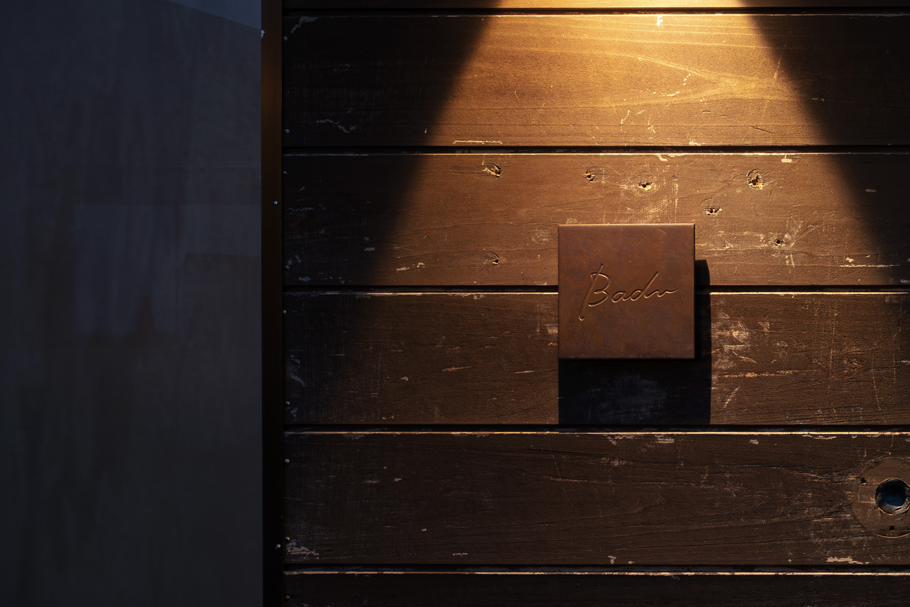 京都・哲学の道近くのレストランBaduの外観サイン。経年した木壁と温かな照明が静かな存在感を放つ。