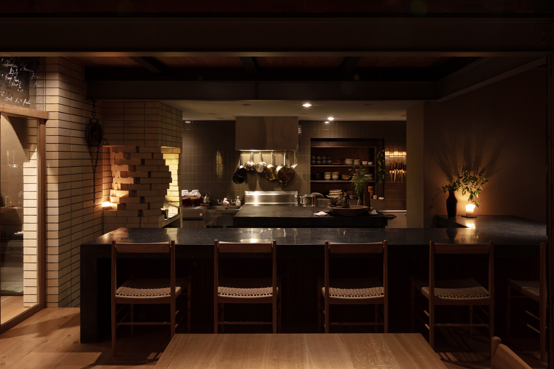 「Badu」のオープンキッチン。左官による研ぎ出しカウンターとレンガの炭焼き台が、料理と建築を結ぶ中心として配置されている。