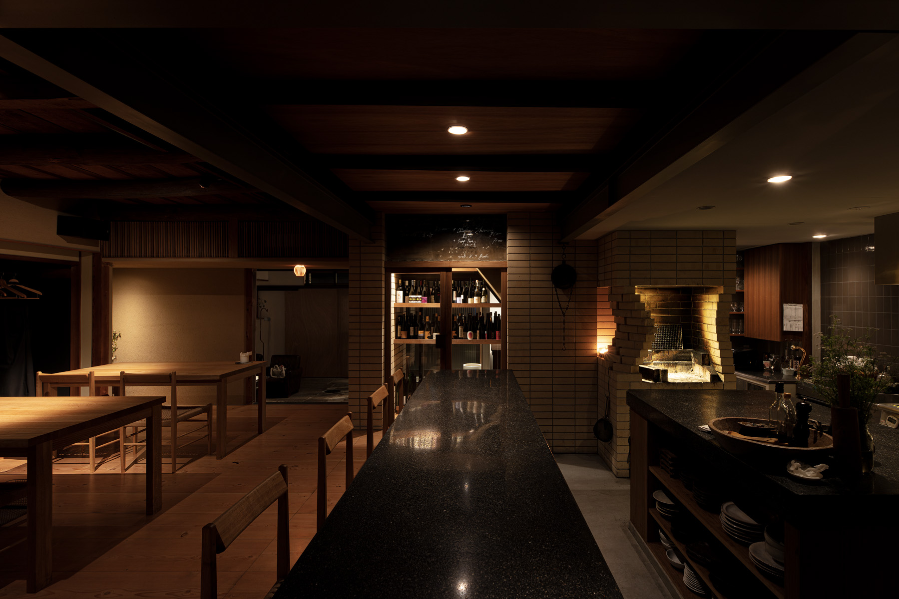 「Badu」のダイニングとキッチン全景。ワインセラーやレンガの炭焼き台が並び、町家の梁や構造を生かした一体的な空間構成。